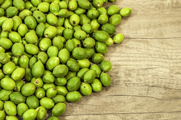 Veel groene jonge walnoten in bolsters op houten tafel — Stockfoto