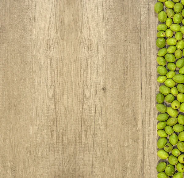 Jeunes noix vertes en cosses sur le côté droit en rangée sur une table en bois — Photo