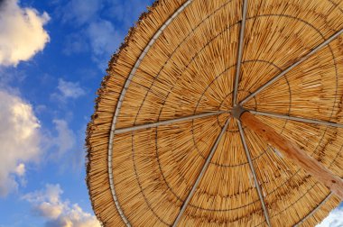Yaz aylarında tatil simgeleyen reed güneş şemsiyesi ve mavi bulutlu bir gökyüzü