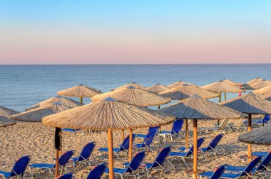 Şezlong, güzel yükselen güneş plaj arka plan üzerinde saman şemsiye