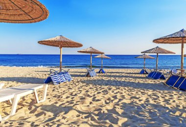 Şezlong, güzel bir plaj arka plan üzerinde saman şemsiye