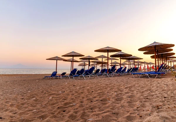 Um monte de espreguiçadeira, guarda-chuva de palha em belo sol nascente praia fundo — Fotografia de Stock