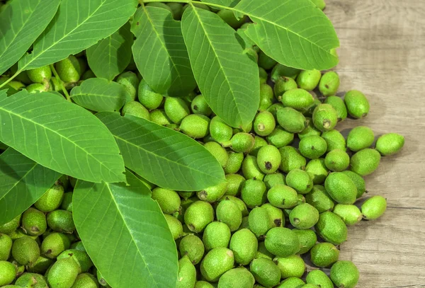 Beaucoup de jeunes noix vertes en cosses sur une table de cuisine avec des feuilles vertes — Photo