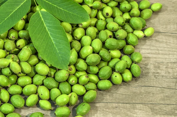 Beaucoup de jeunes noix vertes en cosses sur une table de cuisine avec des feuilles vertes — Photo