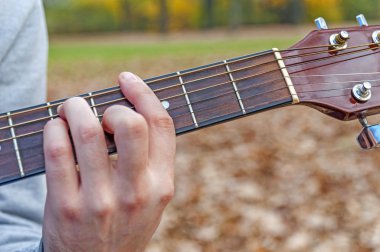 Genç adam akustik gitar çalmak yakın sonbahar Park açık havada çekim