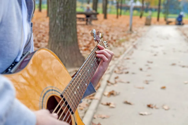 Young man playing acoustic guitar close up outdoors in autumn park — Stock Photo, Image