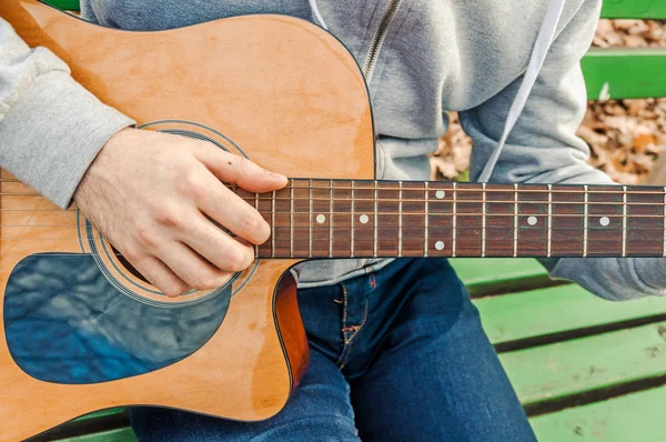 Young man playing acoustic guitar close up outdoors in autumn park — Stock Photo, Image