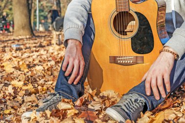 Genç yapraklarda sonbahar parkta oturan ve gitar tutan adam