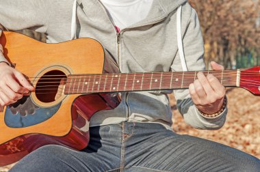 Park ahşap sandalye üzerinde oturan ve gitar çalmak genç adam