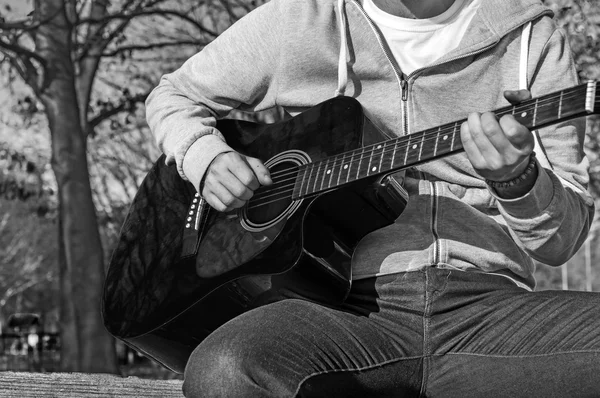 B&W - genç adam Park ahşap sandalye üzerinde oturan ve gitar çalmak