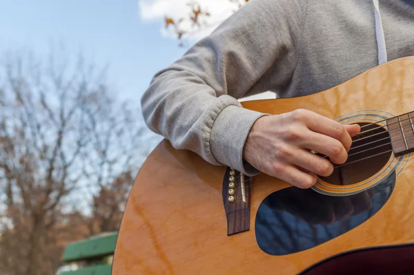 Young man sitting on bench in park and playing guitar — Stock Photo, Image