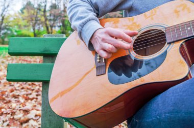 Genç adam akustik gitar çalmak yakın sonbahar Park açık havada çekim