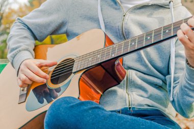 Genç adam sonbahar parkta bankta akustik gitar çalmak