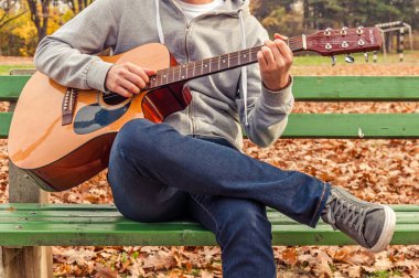 Genç adam sonbahar parkta bankta akustik gitar çalmak