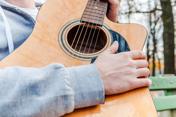 Young man holding acoustic guitar on bench in autumn park — Stock Photo, Image