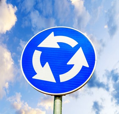 Blue roundabout crossroad road traffic sign against blue cloudy rainy sky clipart