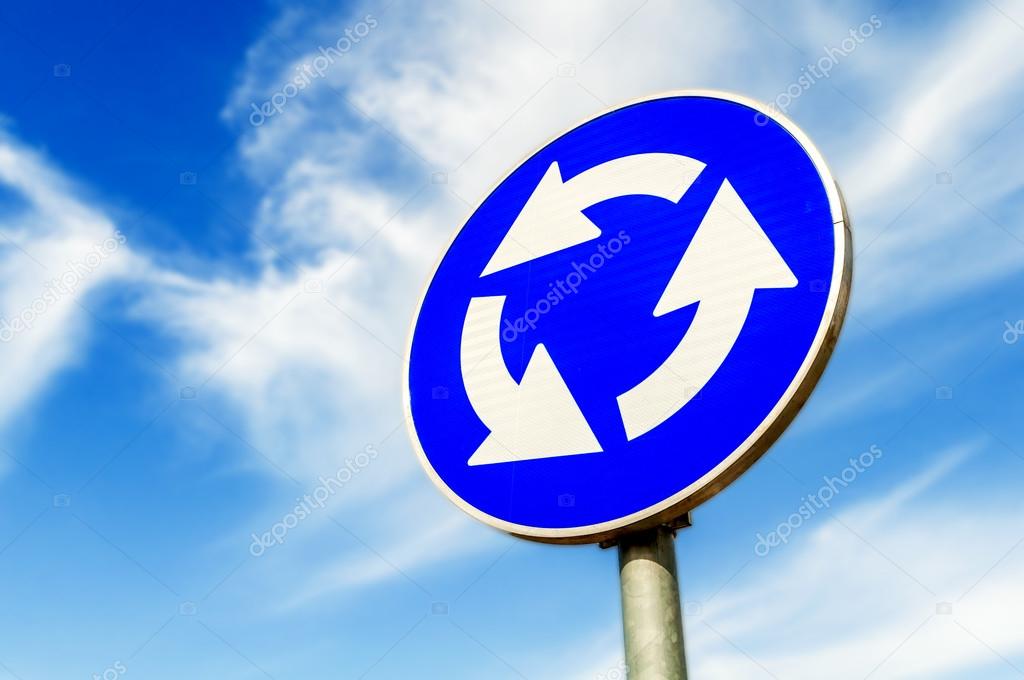 Blue roundabout crossroad road traffic sign against blue sky