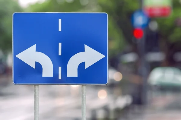 Straßenschild mit gegenläufigen Pfeilen auf zwei Stangen und Straßenhintergrund — Stockfoto