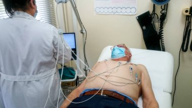 Tanı odasında sedyede yatan yaşlı bir adam kardiyograma bağlı.