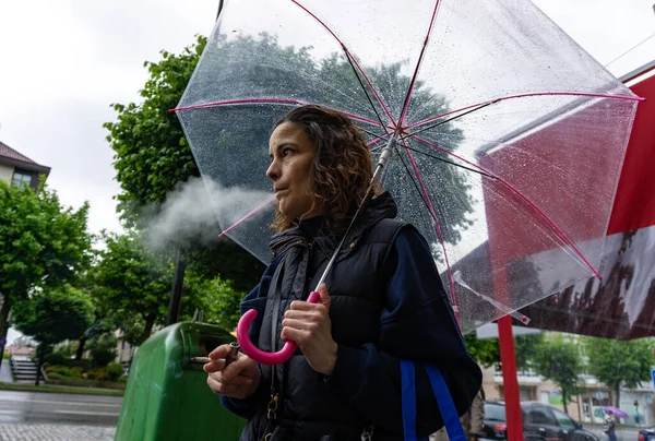 Sokakta elinde su damlalarıyla sigara içen bir kadın.