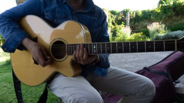 Adam bahçede oturup akustik gitar çalıyor.