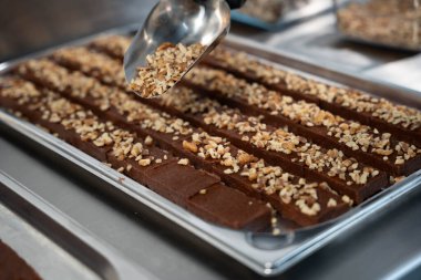 Çelik bir yüzeydeki kakao macununu işlemek için metal bir silindir kullanan eldivenli ellerin yakın çekimi. Çikolata yapma sürecinin ayrıntıları.