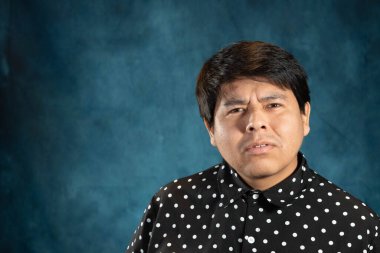 Close-up portrait of a man in a black polka dot shirt. Pose with a serious and determined expression on a textured blue background with dramatic studio lighting.