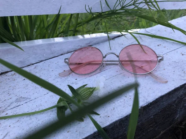 Çimlerin yanındaki beyaz bir tahta parçasına pembe gözlük.