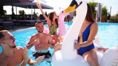 Arkadaşların havuzda kokteyllerle parti veriyor. Mayo dansındaki mutlu gençler, güneşli bir günde şişme flamingo, kuğu ve şilte ile gece kulübü. Yavaş çekim
