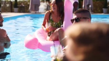 Arkadaşların havuzda kokteyllerle parti veriyor. Mayo dansındaki mutlu gençler, güneşli bir günde şişme flamingo, kuğu ve şilte ile gece kulübü. Yavaş çekim