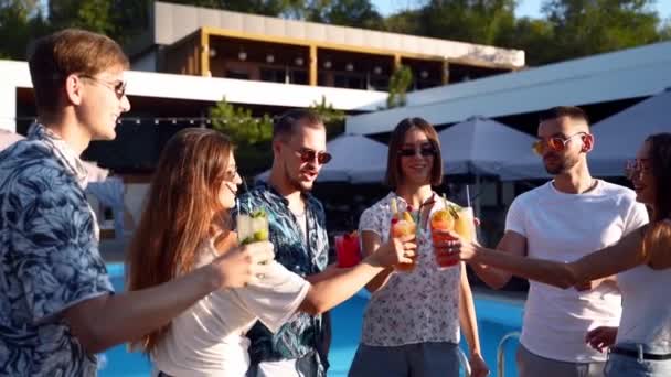 Eine Gruppe von Freunden vergnügte sich bei einem Sommerfest am Pool und klapperte Gläser mit Sommercocktails an einem sonnigen Tag in der Nähe des Schwimmbades. Menschen stoßen in Zeitlupe mit frischem Saft in tropischer Luxusvilla an. — Stockvideo