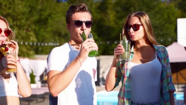 Group of friends having fun at poolside summer party clinking glasses with colorful cocktails and putting them on a table. People toast drinking fresh juice at luxury tropical villa in slow motion. — Stock Video