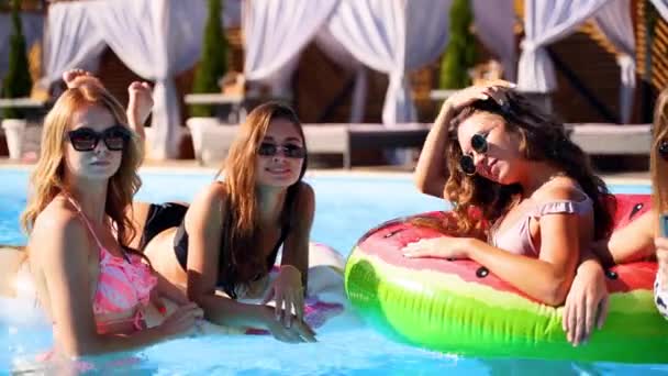 Belles jolies filles chaudes en bikini prenant selfie dans la piscine sur flottant de pastèque gonflable. Femmes équipées en maillots de bain faisant des photos sur la caméra smartphone lors de la fête d'été ensoleillée de la journée. Mouvement lent — Video