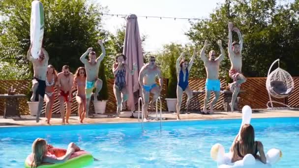 Счастливые друзья прыгают и плещутся в бассейне с надувными поплавками на роскошном курорте. Молодые люди в купальниках устраивают вечеринку на частной вилле для отдыха. Горячие девушки прыгают в воду. Медленное движение. — стоковое видео