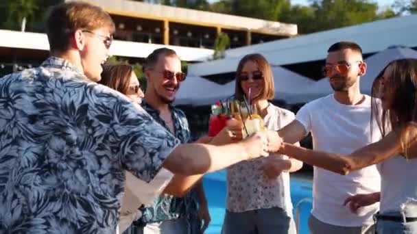 Eine Gruppe von Freunden vergnügte sich bei einem Sommerfest am Pool und klapperte Gläser mit Sommercocktails an einem sonnigen Tag in der Nähe des Schwimmbades. Menschen stoßen mit frischem Saft in Luxusvilla auf Tropenurlaub an. — Stockvideo