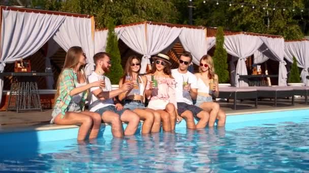 Vriendengroep die zich vermaken op een feestje bij het zwembad met glazen met verse cocktails zittend bij het zwembad op zonnige zomerdag. Mensen proosten drankjes in luxe villa op tropische vakantie. — Stockvideo