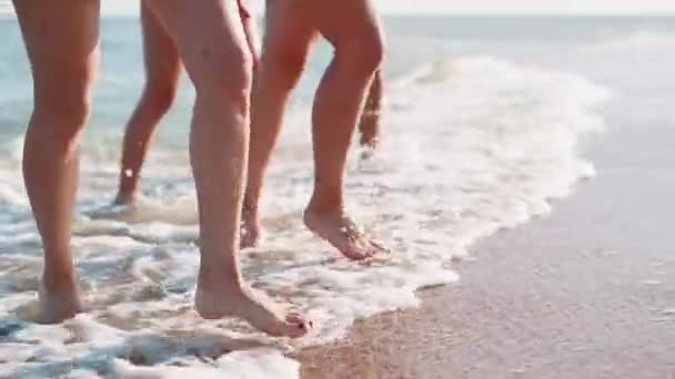 Slanke vrouwelijke poten en voeten lopen uit de golven van zeewater op zandstrand. Mooie vrouwen gaan naar de kust. Spatten water en schuim in 120 fps slow motion. Meisjes na het baden in de oceaan gaan naar de kust. — Stockvideo