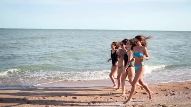 Eine Gruppe hübscher Freundinnen läuft in Badeanzügen am Meer entlang am tropischen Sandstrand. Interrassische Frauen im Bikini haben Spaß beim Bräunen an einem Sommertag im Freien. Mädchen in Badebekleidung laufen in Zeitlupe. — Stockvideo