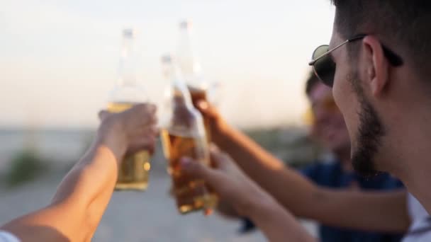 Группа друзей веселятся тосты, пить пиво, отдыхать на морском пляже на закате в замедленной съемке. Молодые мужчины и женщины наслаждаются напитками, сидя на песке на теплой летней вечеринке. Люди с лимонадом. — стоковое видео