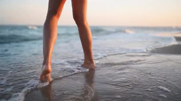 Slim gambe femminili e piedi che camminano lungo onde d'acqua di mare sulla spiaggia di sabbia. Bella donna cammina al mare surf. Schizzi d'acqua e schiuma in 120 fps al rallentatore. Ragazza dopo il bagno in oceano andare a riva. — Video Stock