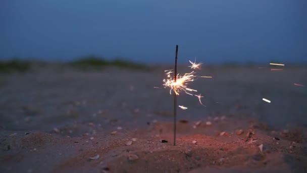 Sparkler bastone in sabbia da spiaggia, bruciare quasi a finire al tramonto al tramonto. Brillanti scintille volano intorno, illuminano la superficie con luce calda. Movimento lento di scintille che emettono fuochi d'artificio che bruciano nel suolo all'aperto. — Video Stock