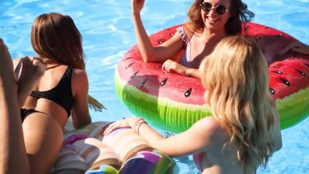 Vakre, pene jenter i bikini har bassengdans med oppblåsbar vannmelon- madrass. Glamour-antatte kvinner i badetøy, solbriller har det gøy med å slappe av, klubbe på solfylte sommerdager. – stockvideo