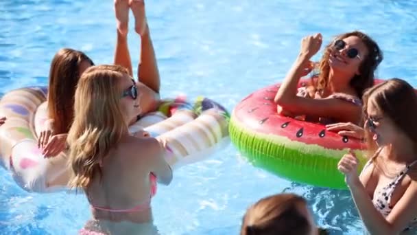 Amigos tienen fiesta en una piscina villa privada. Jóvenes felices en trajes de baño bailando, uniéndose y follando con flotadores y colchones inflables en un resort de lujo en un día soleado. Movimiento lento. — Vídeos de Stock