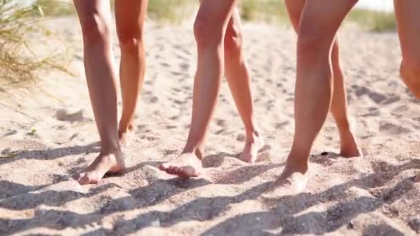 Vista da vicino delle donne abbronzate gambe e piedi che camminano sulla spiaggia sabbiosa verso l'oceano nella giornata di sole. Slim belle ragazze vanno al mare sulla sabbia bianca chiara. Amici in vacanza. Angolo telecamera basso, rallentatore. — Video Stock
