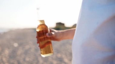 Gün batımında yavaş çekimde kumsalda cam şişe bira içen yakışıklı beyaz bir adam. Erkek, kumlu deniz kıyısında limonata ile susuzluğunu giderir. Güneş patlamaları, takip çekimi..