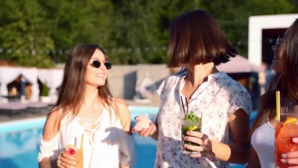 Grupo de chicas divirtiéndose en la fiesta de la piscina de verano, tintineando vasos con cócteles y bailando cerca de la piscina del hotel al aire libre. Mujeres brindan bebiendo jugo en villa de lujo en cámara lenta . — Vídeo de stock