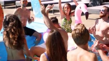 Arkadaşlar özel bir villada yüzme havuzunda parti yaparlar. Güneşli bir günde mayo giyen, dans eden, şamandıralarla takılan ve lüks bir tatil köyünde şişme yatak giyen mutlu gençler. Yavaş çekim.
