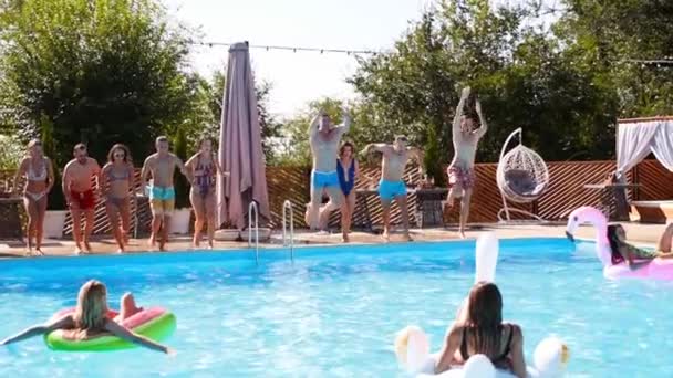 Amici felici che saltano e schizzano in piscina con carri gonfiabili in resort di lusso. Giovani in costume da bagno che fanno festa in villa privata. Le ragazze calde saltano in acqua. Rallentatore. — Video Stock