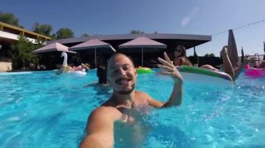 Yaşam stili blogcusu yüzme havuzunda kamerayla selfie çekiyor. Lüks oteldeki partiden seyahat vlogger filmleri. Sosyal medya beğenileri için canlı yayın yapan uygun bir adam. Yavaş çekim.