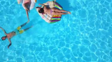 Havadan. Arkadaşlar şişme flamingo, kuğu, şamandıra ve şezlonglara bronzlaşırlar. Lüks otellerdeki şişme yataklarda banyo yapan mutlu gençler. Yukarıdan bak. Bikinili kızlar güneşte güneşleniyor.